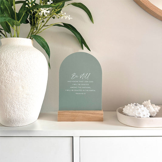 Be Still Bible verse Psalm 46:10 Verse & Oak scripture stand with handcrafted Tasmanian oak base, styled on a white cabinet beside a large white vase with greenery and a dish of white coral.