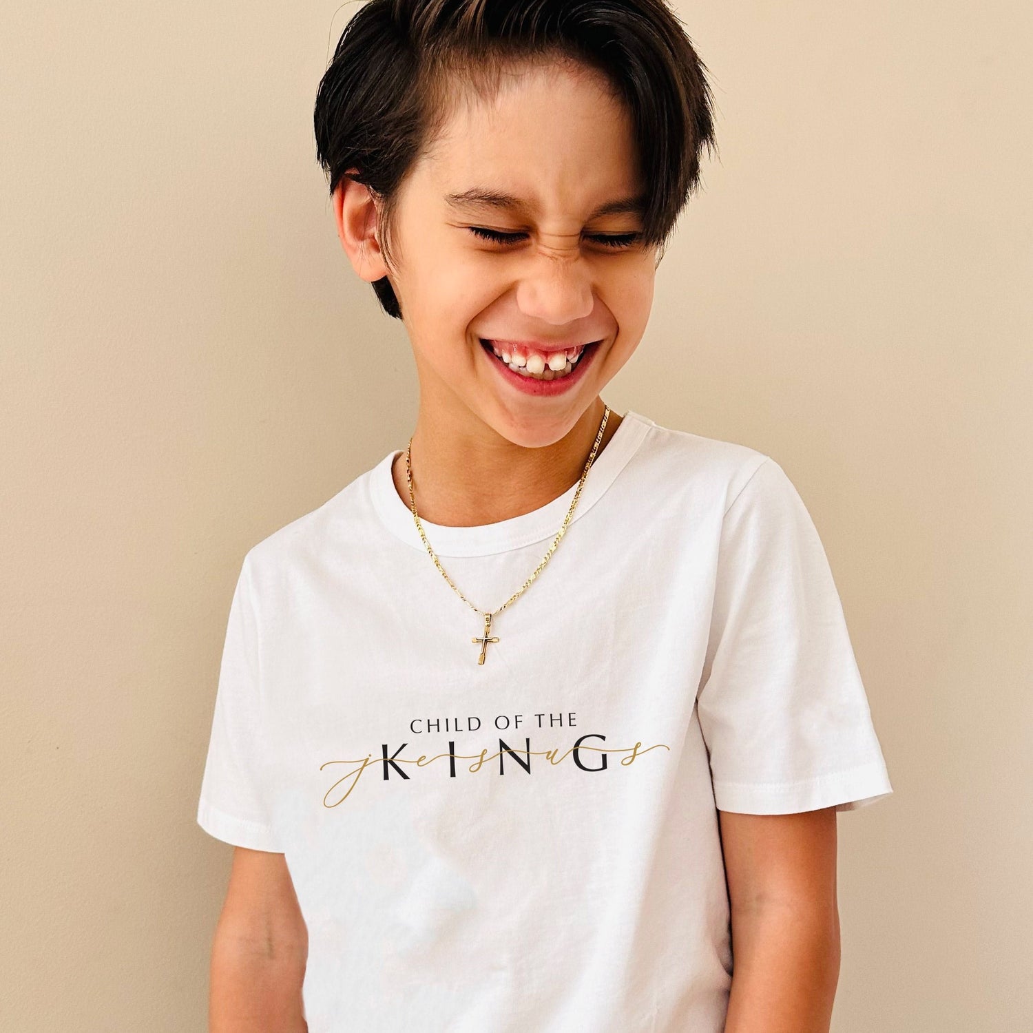 Young boy wearing 'Child of the King' christian tee in white cotton. The design features the word Jesus in gold weaved through the design.