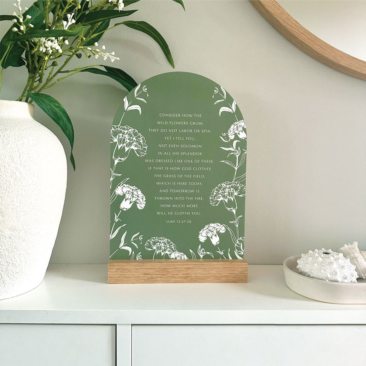 Wildflowers Luke 12:27–28 Verse & Oak stand - features the bible scripture with white floral illustrations against grass green with a handcrafted Tasmanian oak base. Styled on a white shelf with decorative vase and coral.