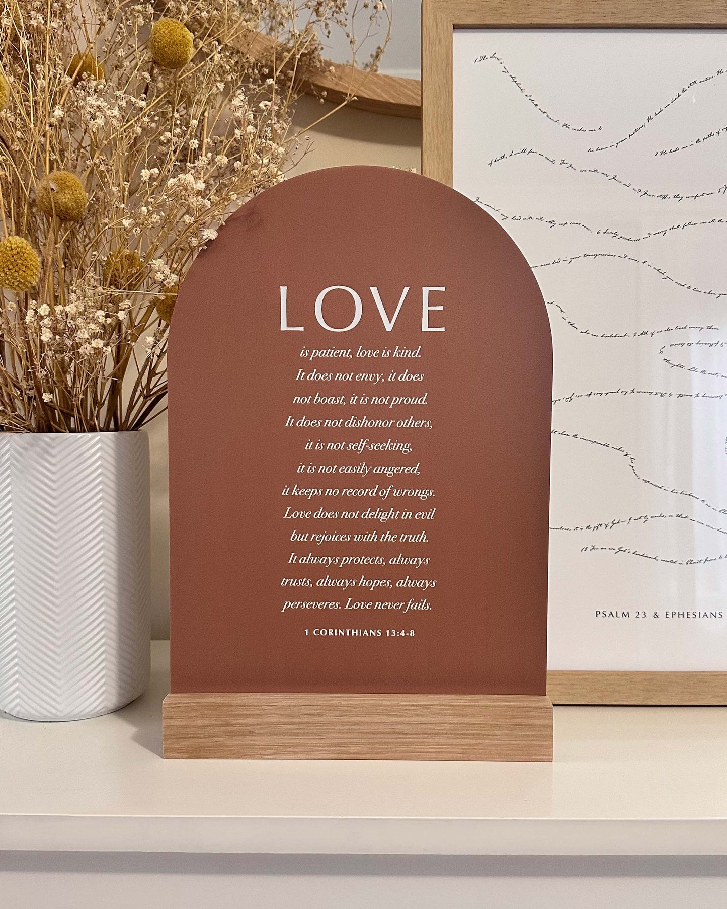 Decorative sign with 'LOVE' text on a shelf with plants and framed picture